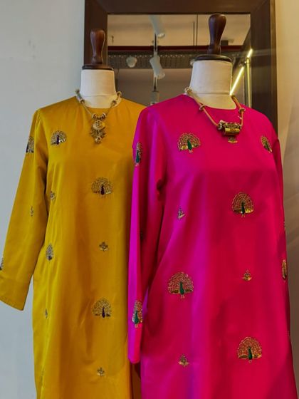 Two beautiful silk kurtas from Raw Mango, one in mustard yellow and the other in fuchsia pink, both adorned with delicate peacock embroidery.