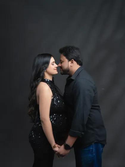 An intimate nose-to-nose pose. This close-up shot captures the deep affection and connection between the parents-to-be in a simple, dark studio setting.