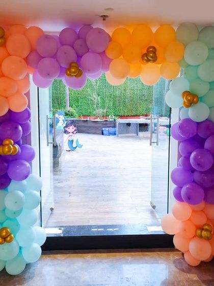 A vibrant balloon archway in orange, purple, and teal, creating a colorful entrance for a mermaid-themed party.