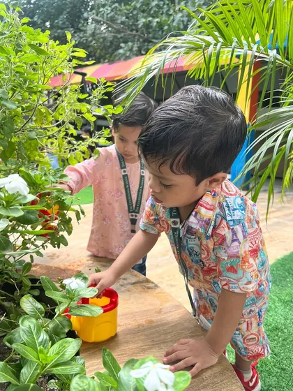 A moment of gentle exploration. This little one is not just watering the plant but also observing it closely, a sign of a curious and engaged mind.