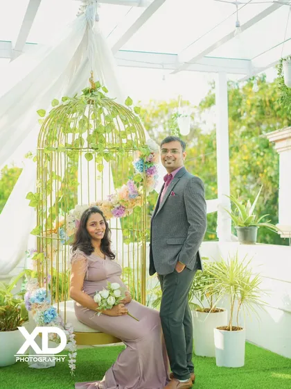 An elegant indoor studio portrait featuring a golden birdcage swing and beautiful floral arrangements.