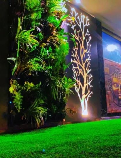 A stunning night view of the Gurgaon project, featuring backlit tree art, a vertical garden, and a Buddha art piece, creating a dramatic and artistic wall.