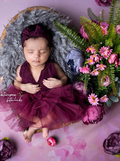 A sleeping newborn in a purple dress, nestled in a heart-shaped basket with flowers. A beautiful composition celebrating new love.