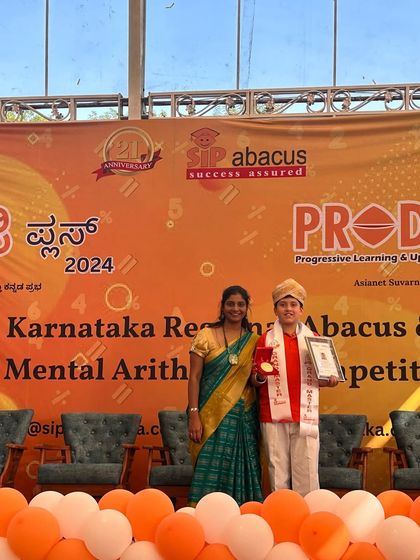 A student stands proudly with his teacher and his award at the Prodigy Plus 2024 event. This one on one recognition is a special moment for every achiever.