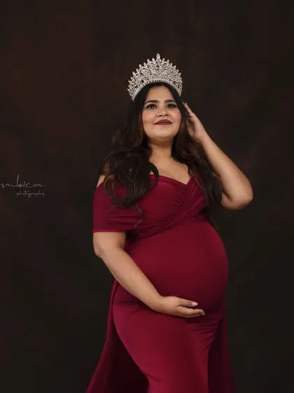 A classic portrait from the "Queen" session, focusing on her radiant and confident expression. The rich red gown and sparkling crown make for a powerful and glamorous maternity look.