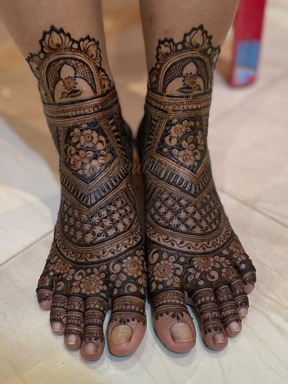 A beautiful lotus-themed bridal foot design. The top of the feet feature a lotus in a dome, with floral bands and checkerboard patterns completing the look down to the toes.