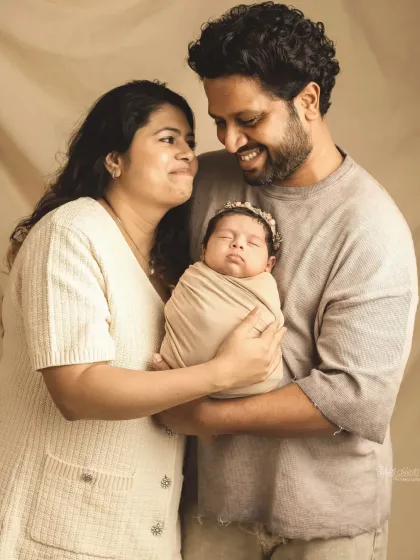 A happy family portrait, with both parents smiling as they hold their sleeping newborn.