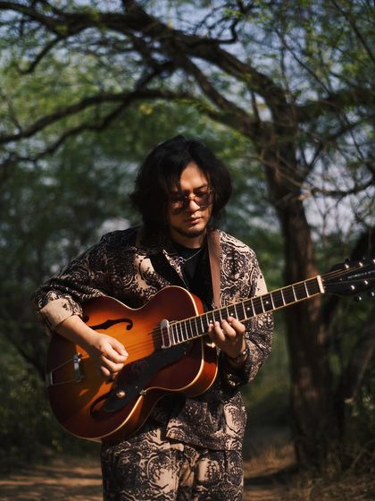 Taba Chake with his guitar in a forest clearing. This image connects the artist to nature, the source of so much inspiration.