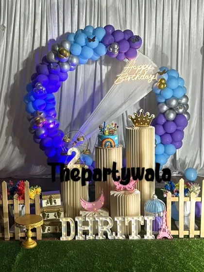 A stylish ring decoration with blue, purple, and silver balloons against a green turf floor. The picket fence and light-up name complete the look.