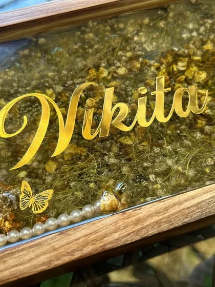 A close-up of the wooden nameplate, showing the detail of the preserved flowers and the elegant gold lettering of the name 'Nikita'.