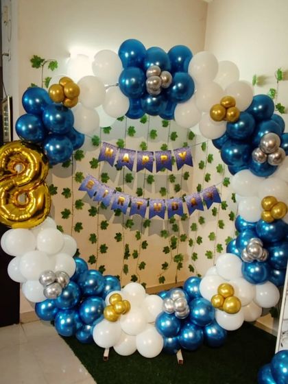 An 8th birthday decoration with a blue, white, and gold balloon ring. The setup includes a large foil number '8' and a 'Happy Birthday' banner.