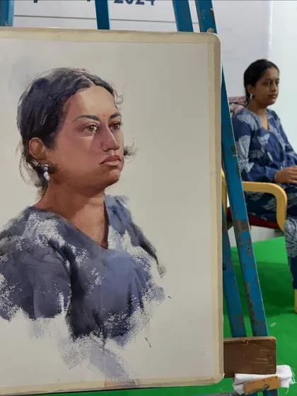 The finished watercolour portrait on the easel, with the model seated in the background for comparison.
