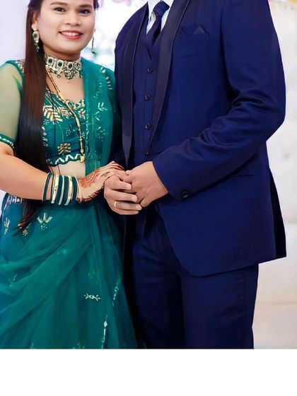 A beautiful pairing for a reception or engagement. She is wearing a stunning green lehenga with intricate work, and he is in a classic navy blue tuxedo. The contrast is elegant and timeless.