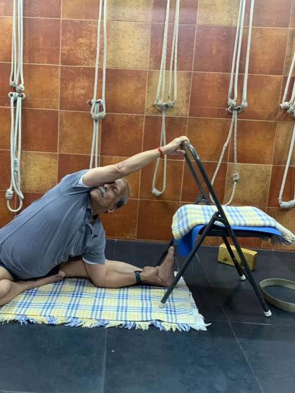 A seated forward bend (Janu Sirsasana) using a chair for support. This is a common pose we explore in online classes to work on hamstring and spine flexibility.