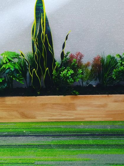 A custom-built wooden planter box for an office. It's filled with a mix of colorful artificial plants, including a snake plant, to brighten up the workspace.