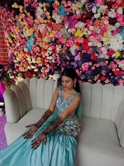A stunning bride seated against a wall of flowers, her mermaid-themed mehndi perfectly matching her enchanting look.