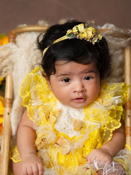 A curious and wide-eyed look from a baby celebrating her 100-day milestone. The warm yellow flowers and rustic props create a cozy and beautiful setting.