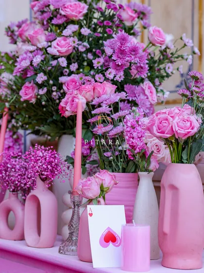 More unique vase shapes, including a face-shaped vase and modern loop designs, all in shades of pink. The ace of hearts card adds a whimsical, romantic touch to the arrangement.