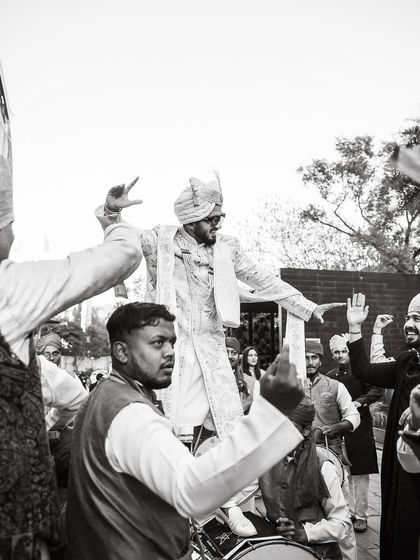 Bringing the beats to the baraat. A classic black and white shot of the groom dancing on the dhol player's shoulders.