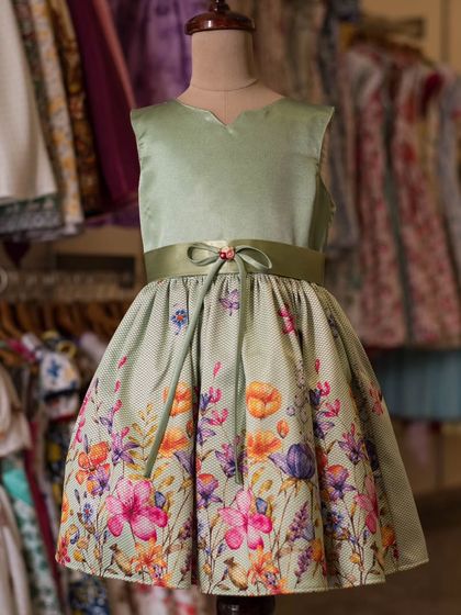 A mannequin displaying the beautiful wildflower border print dress. The background shows a rack of other colorful options available in my studio.
