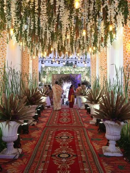 The guest's journey is part of the experience. We designed this beautiful entrance aisle with a ceiling of hanging white florals and Edison bulbs, flanked by tall grasses to create an immersive, rustic-glam pathway.