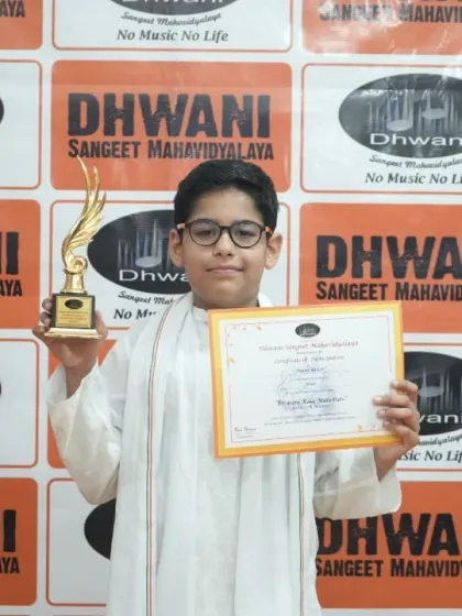 A proud student in traditional kurta holds his certificate and trophy.