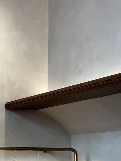 A detail of a carved wooden shelf against a lime-washed wall at the Eka store. The lighting is designed to be soft and ambient, highlighting the textures of the materials and the craftsmanship of the fixtures.
