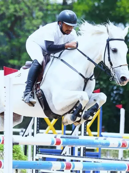 A stunning white horse and rider soar over a jump during the Karnataka State Equestrian Competition. This image showcases the power and grace we train for.