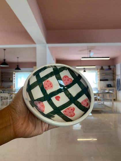A hand-painted bowl with a playful checkered and heart pattern, created by a student in our Paint-A-Pot session.