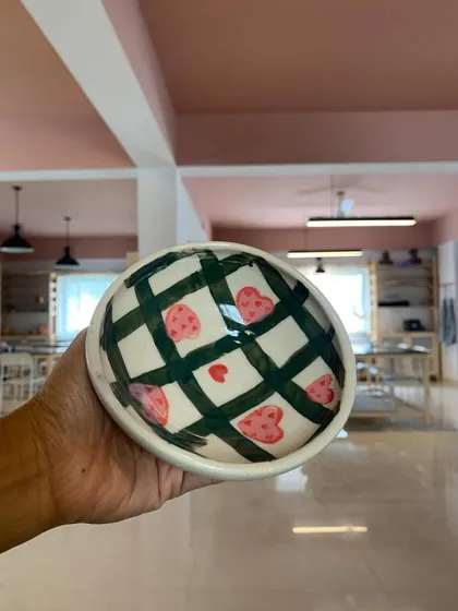 A hand-painted bowl with a playful checkered and heart pattern, created by a student in our Paint-A-Pot session.