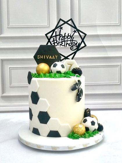 A goal-worthy cake for a young football fan. This design features a hexagonal football pattern, edible soccer balls, and a personalized "Happy Birthday" topper, making it the perfect treat for a sports-themed party.