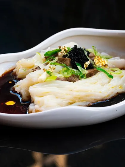 An elegant plating of Cheung Fun (rice noodle rolls) with caviar and gold leaf. The high-end ingredients are highlighted by the clean, sophisticated photography.