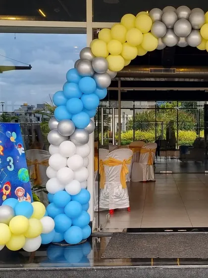 An outer space-themed balloon arch in yellow, blue, white, and silver for a 3rd birthday party.