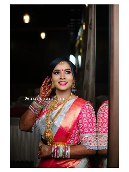 A happy bride getting ready for her big day. She is wearing a custom blouse with geometric embroidery in pink and white, designed to match her beautiful silk saree.