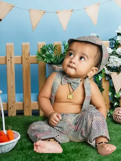 A seven-month-old baby boy in a charming gardener outfit. The setup includes a picket fence, watering can, and a basket of tiny carrots for a cute, rustic feel.