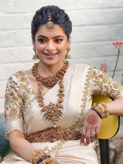 An elegant bridal portrait in a white and gold Kanjeevaram saree. The makeup is soft and natural, with antique gold jewelry completing this classic South Indian look.