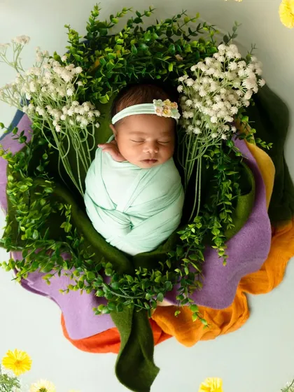 An artistic overhead shot of a newborn swaddled in mint green, nestled within a wreath of fresh greenery and flowers. This composition highlights my attention to color, texture, and detail.