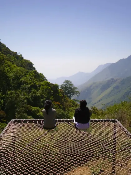 Two trekkers relaxing on a net bed overlooking the vast mountain ranges of Munnar.