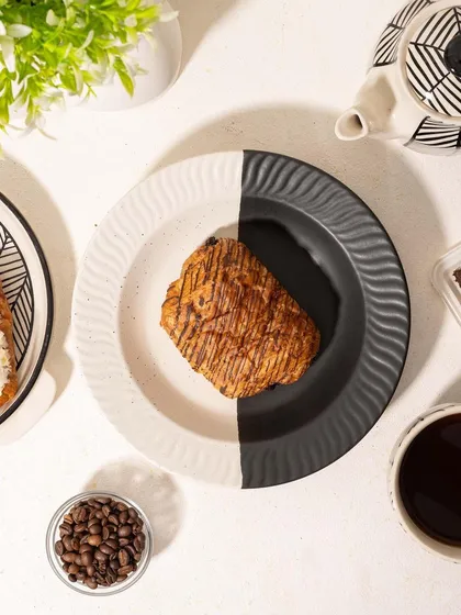 A before-and-after style shot for Homesmith, showing a modern black-and-white plate first empty, then with a croissant. This interactive concept is engaging for social media and shows the crockery's use.