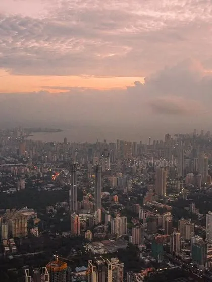 A high-altitude, bird's-eye view of the entire Mumbai peninsula, showing the vast cityscape under a cloudy sky.