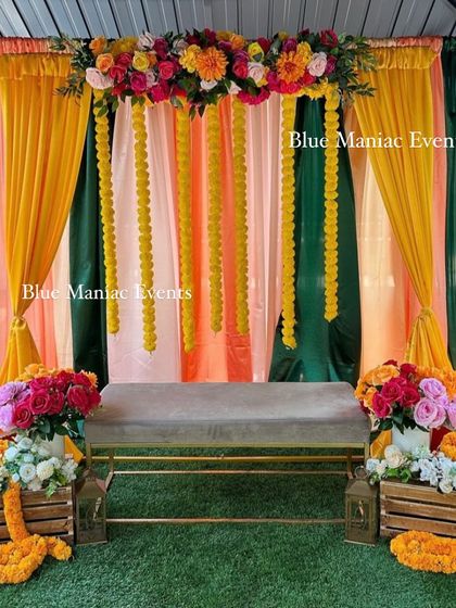 A beautiful outdoor Mehendi setup with a canopy of colorful drapes and hanging marigold garlands. The rustic wooden crates with flowers add a charming touch.