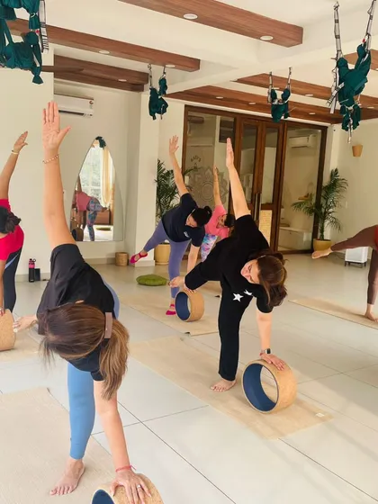 A group of smiling students in a wheel-assisted triangle pose, demonstrating the fun and supportive atmosphere of our classes.