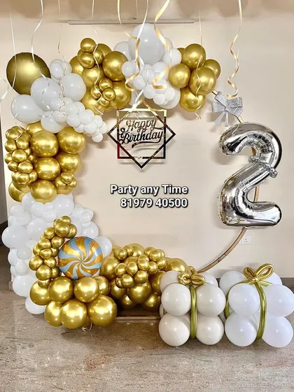A unique birthday setup with a white and gold balloon arch in the shape of a gift box.