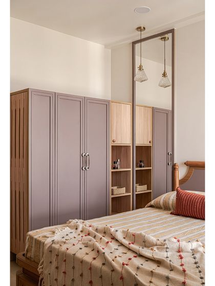 This wardrobe combines mauve-painted shutters with open oak shelving and a full-height mirror. The mix of closed and open storage adds functionality while making the room feel more spacious.
