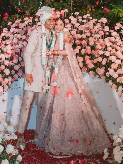 The varmala stage is pure magic. The couple is showered with petals, framed by a beautiful arch of pink and white flowers, a perfect match for this unforgettable wedding moment.
