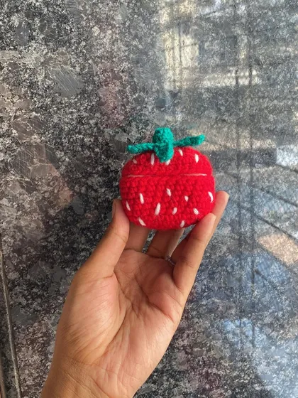 A view of the closed crochet strawberry AirPod case. The green top and white seed details make it look just like a real strawberry.