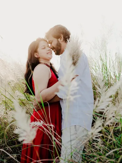 A romantic embrace surrounded by tall, feathery grass. The bright backlighting creates a beautiful halo effect, adding a dreamy quality to the image.