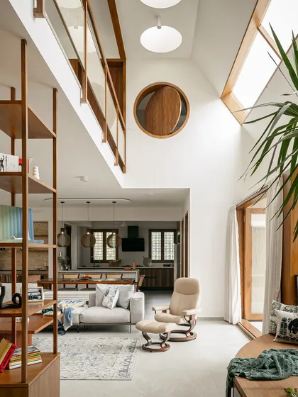 This view showcases the vertical volume of an open-plan living area, connected by a mezzanine bridge. The large circular window is a key architectural feature, drawing the eye upward and flooding the space with sunlight from multiple angles.