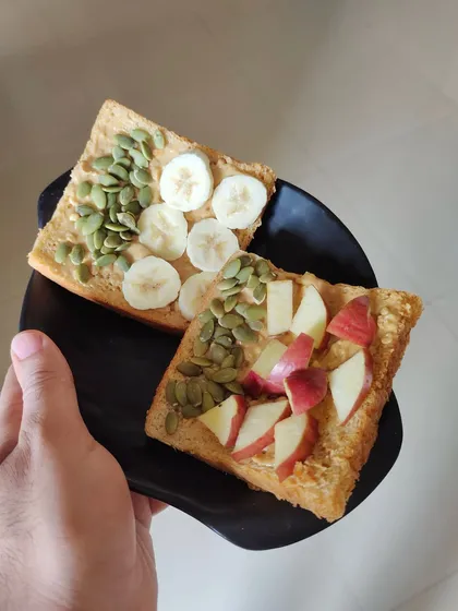A healthy and delicious breakfast or snack: brown bread toast with peanut butter, topped with banana, apple, and pumpkin seeds.