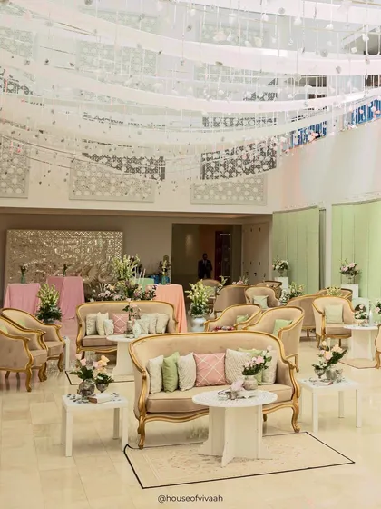 The elegant lounge area for the Haldi, with pastel cushions, gold-trimmed furniture, and a ceiling installation of hanging mirror discs and ribbons.